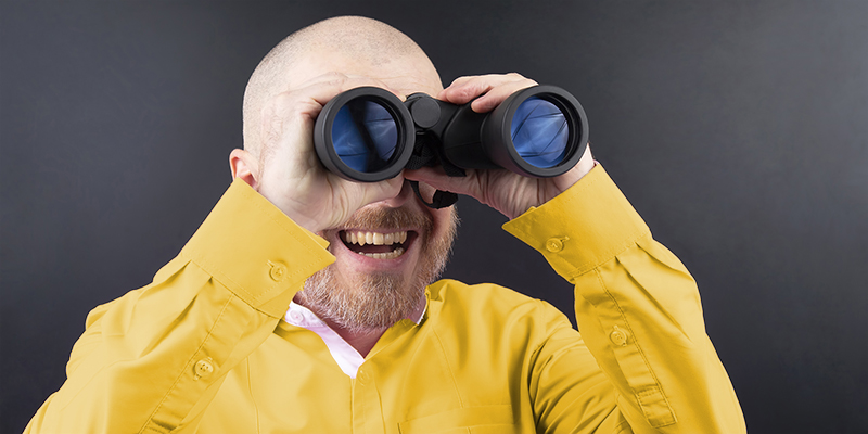 Bearded man looking through binoculars on dark background